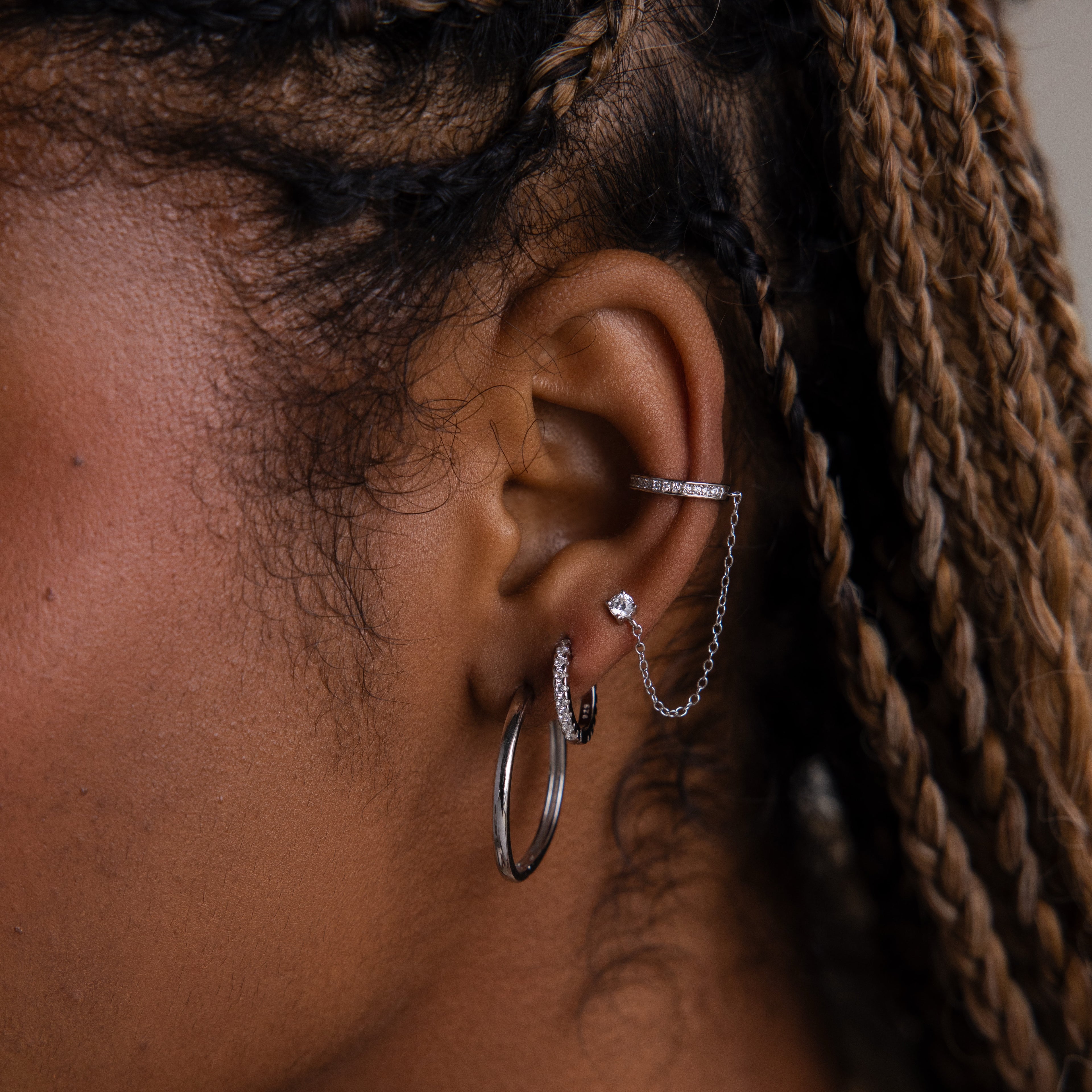 Close-up of an ear with multiple silver earrings against a blurred background