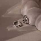 Two silver hoop earrings on a textured beige surface