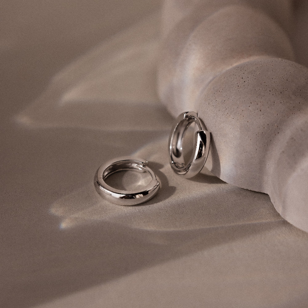 Two silver hoop earrings on a textured beige surface