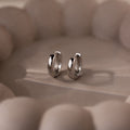 Pair of silver hoop earrings on a textured beige surface
