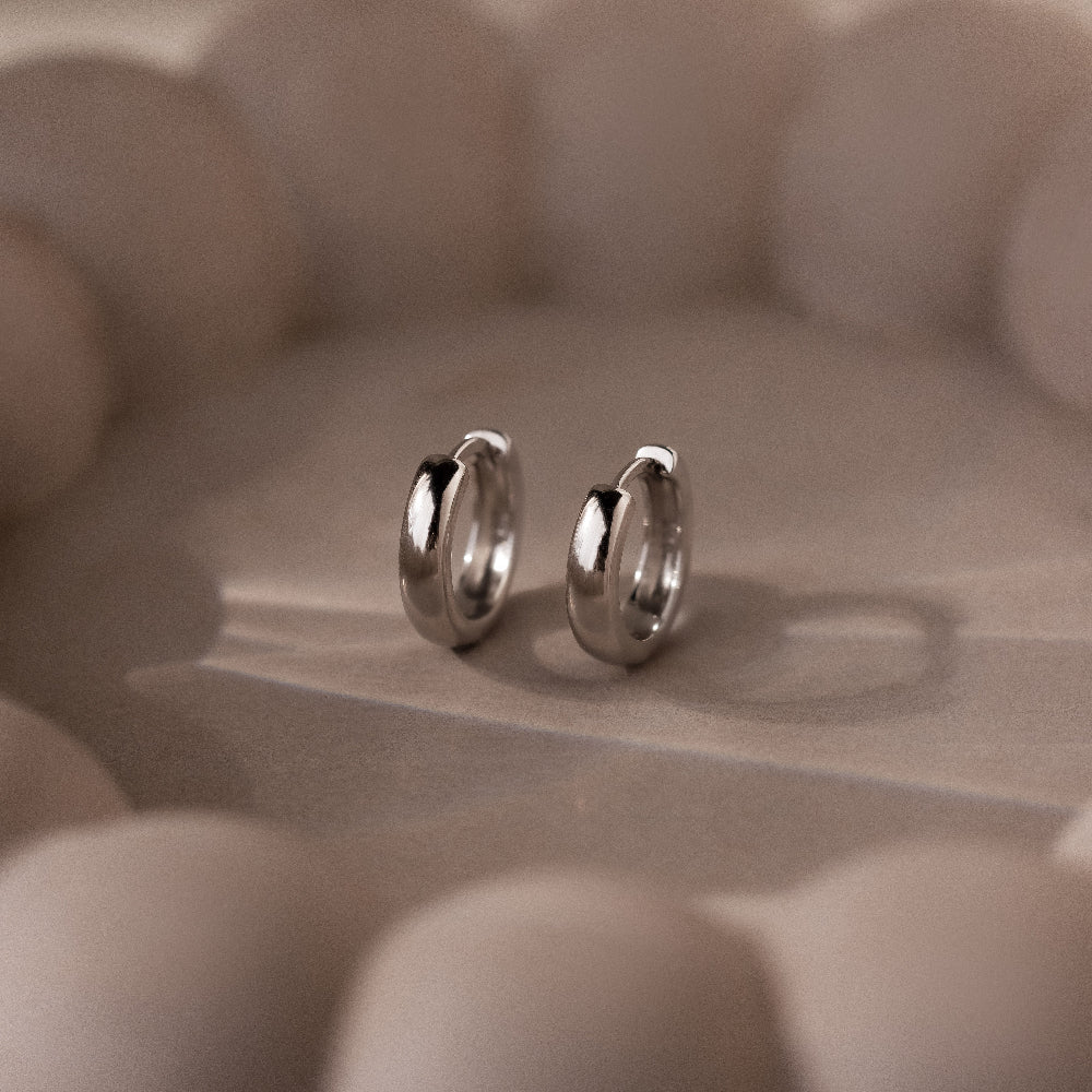 Pair of silver hoop earrings on a textured beige surface
