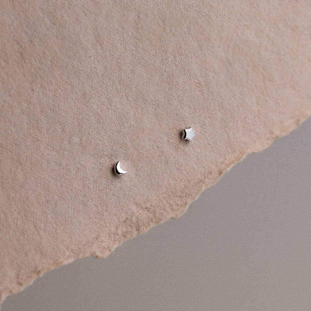 Small star and moon silver earrings on a textured beige surface