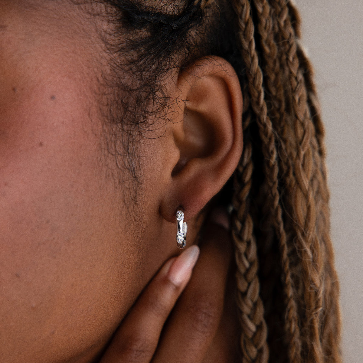 Close-up of a model with a diamond silver hoop earring, hand adjusting hair.