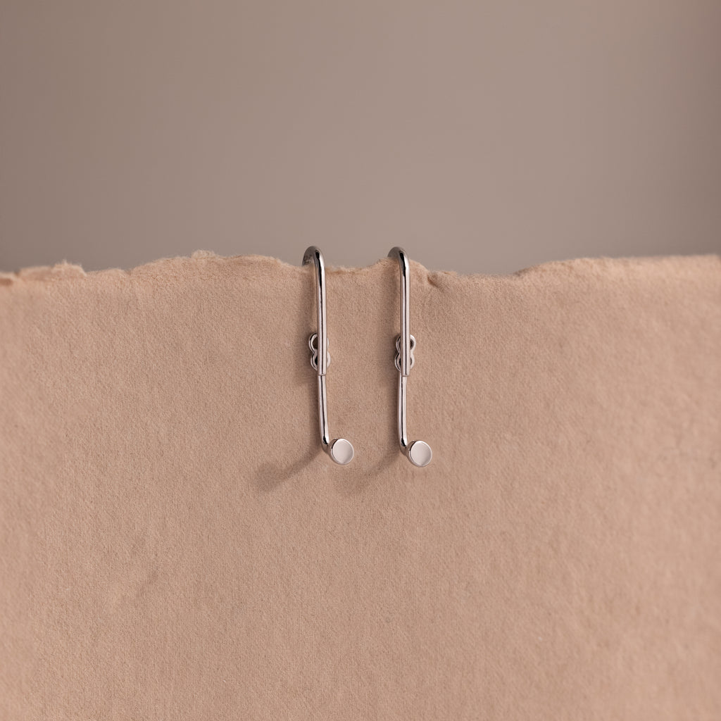 Two silver earring jackets on a beige background