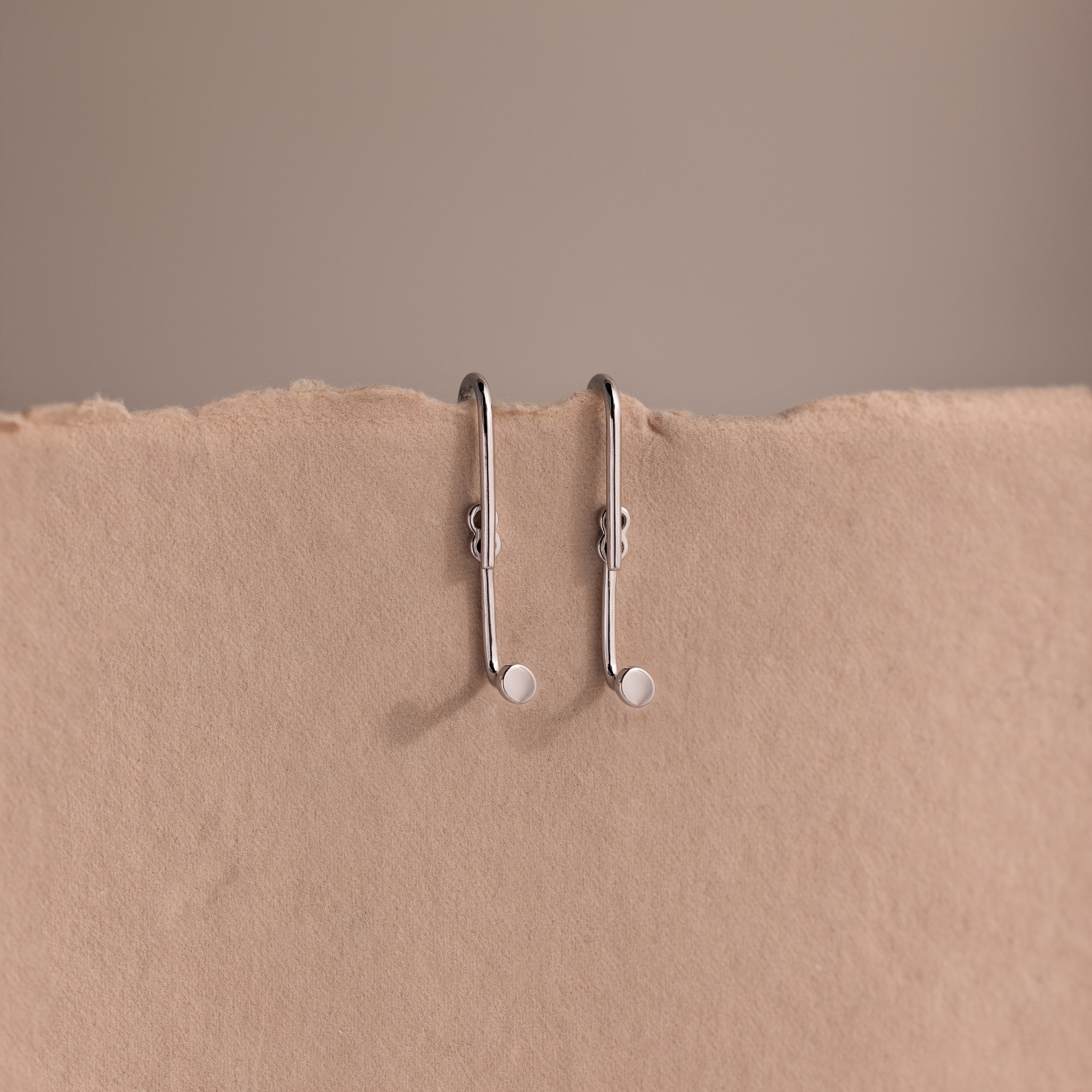 Two silver earring jackets on a beige background