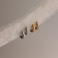 Two pairs of diamond hoop earrings in gold and silver on a textured fabric background.