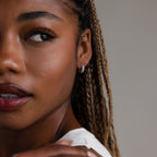 Close-up of a woman with braided hair wearing silver diamond hoop earrings against a neutral background