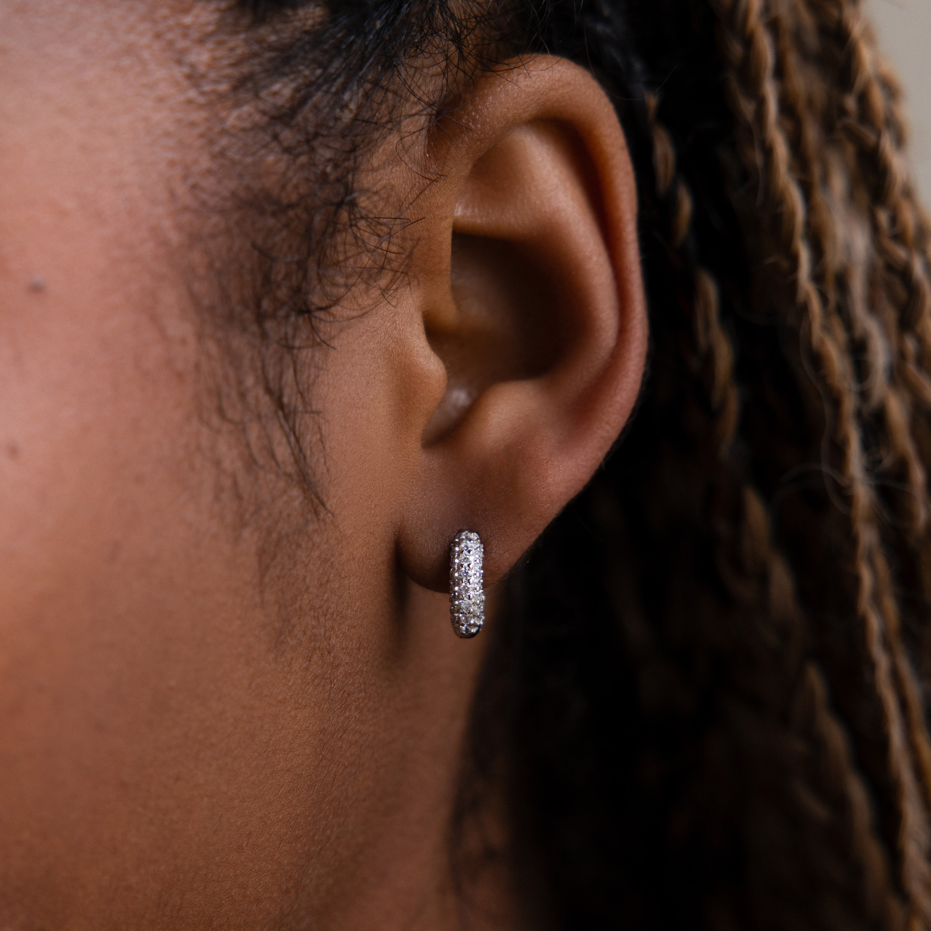 Close-up of a model wearing a silver diamond hoop earring with braided hair.