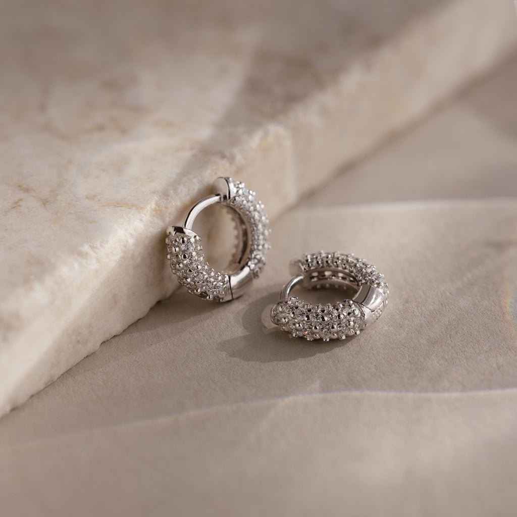 Silver hoop earrings with embedded stones on a beige stone surface