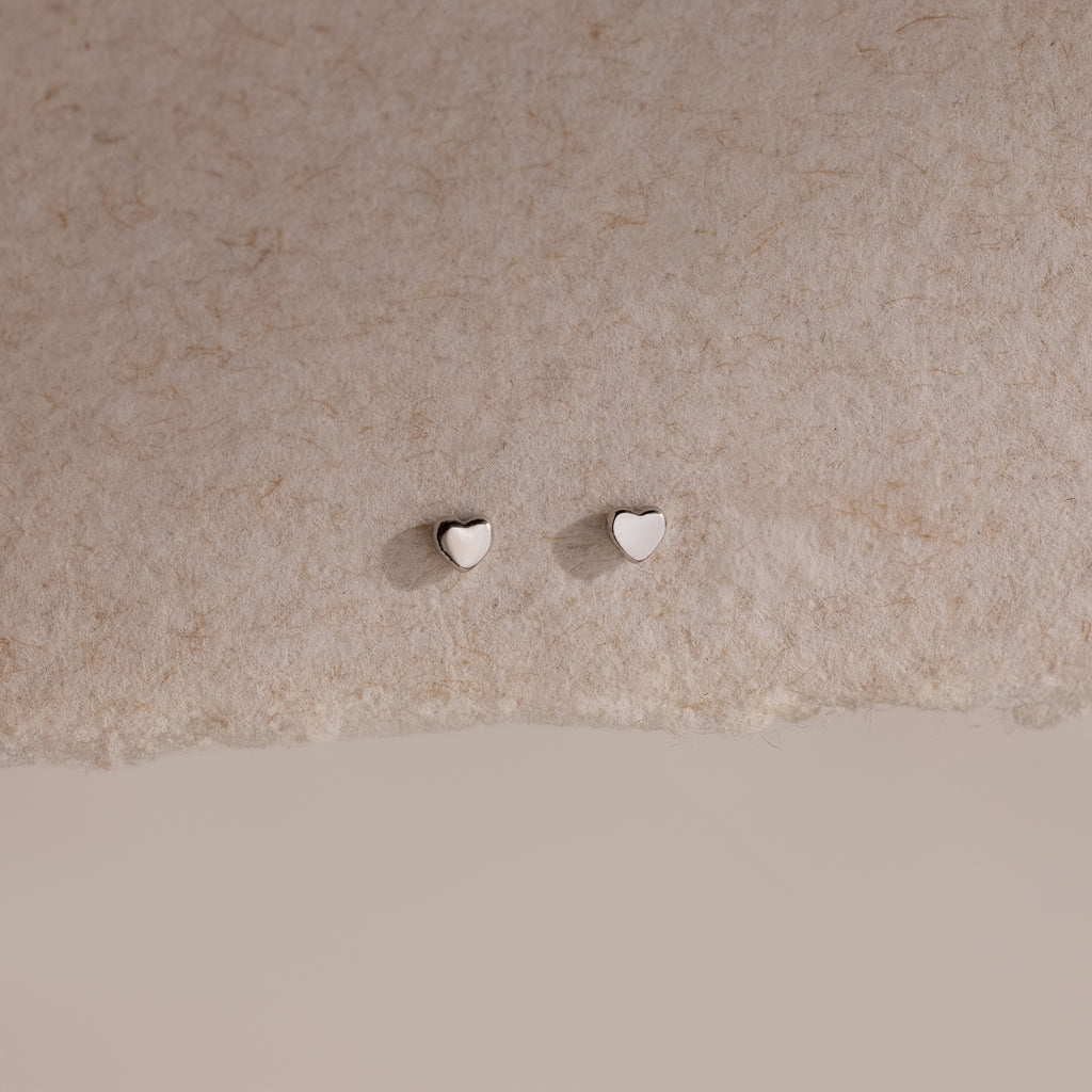 Tiny silver heart-shaped earrings on a beige background