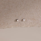 Tiny silver heart-shaped earrings on a beige background