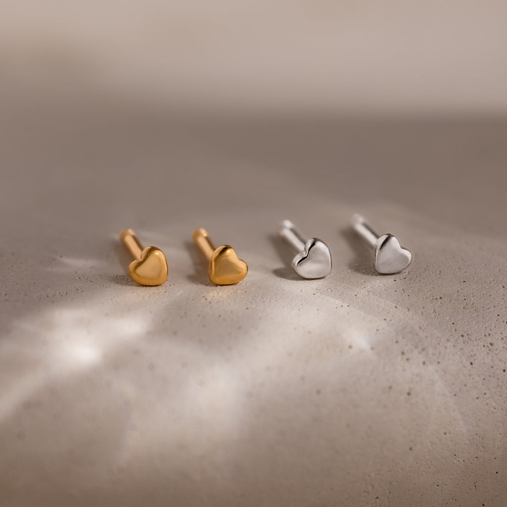 Two pairs of heart-shaped stud earrings, one gold and one silver, on a textured surface.
