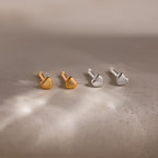 Two pairs of heart-shaped stud earrings, one gold and one silver, on a textured surface.
