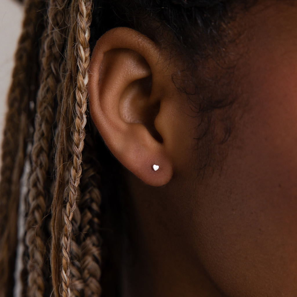 Close-up of a model with a small silver heart stud earring and braided hair.