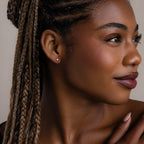 Close-up of a woman with braided hair, tiny silver heart stud earrings, and a neutral background
