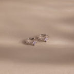 Two Athena Alexandrite Huggies hoop earrings featuring small star-shaped stones are displayed on a beige background with soft shadows—ideal for anyone seeking personalized jewelry with a celestial vibe.