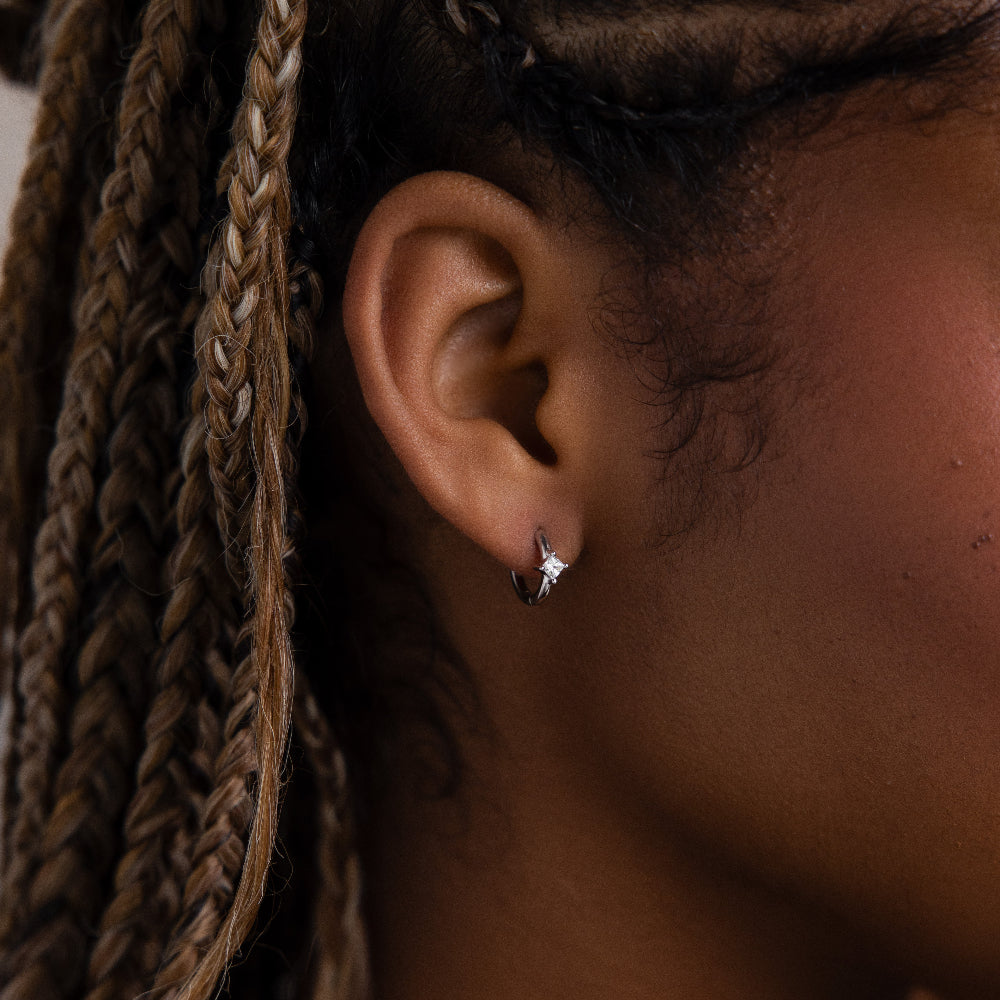 Close-up of a model with a silver huggie hoop diamond earring, braided hair in the background