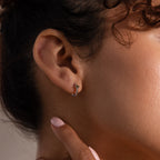 Close-up of a person’s ear wearing Athena Peridot Huggies—small silver hoop earrings with a touch of green—showcasing how personalized jewelry can elevate everyday style.