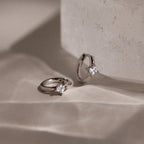 Pair of silver hoop earrings with star-shaped clear gemstones on a textured beige surface.