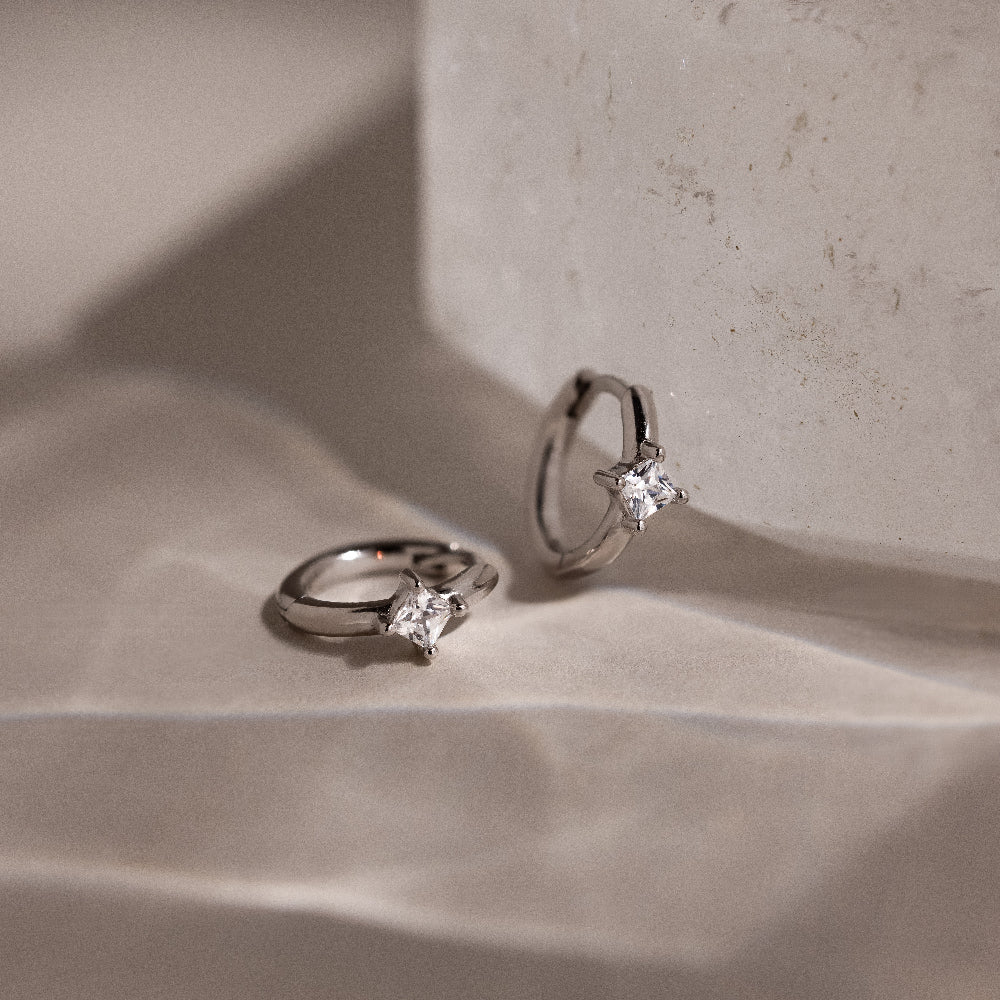 Pair of silver hoop earrings with star-shaped clear gemstones on a textured beige surface.