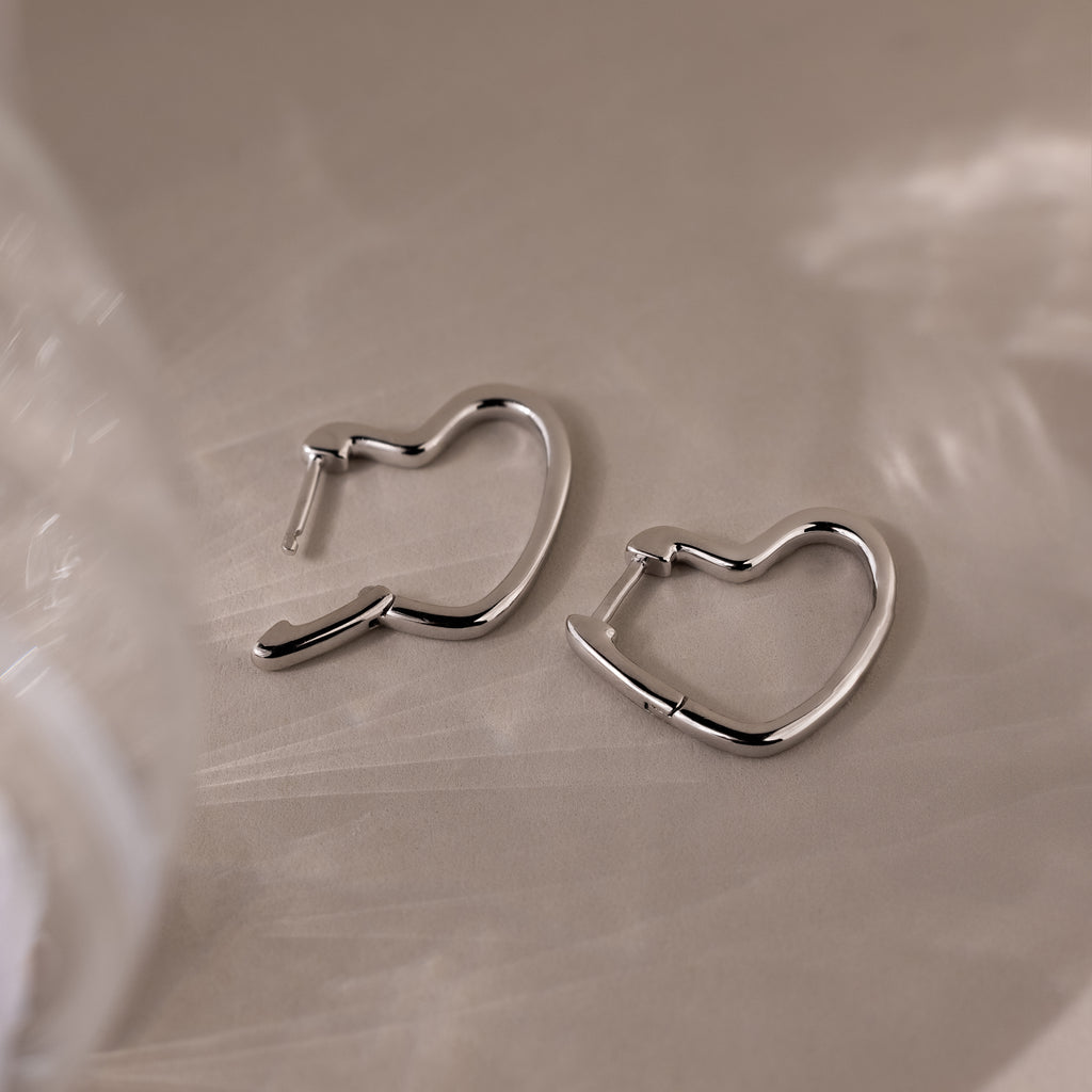 Heart-shaped silver hoop earrings on a beige surface