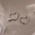 Heart-shaped silver hoop earrings on a beige surface