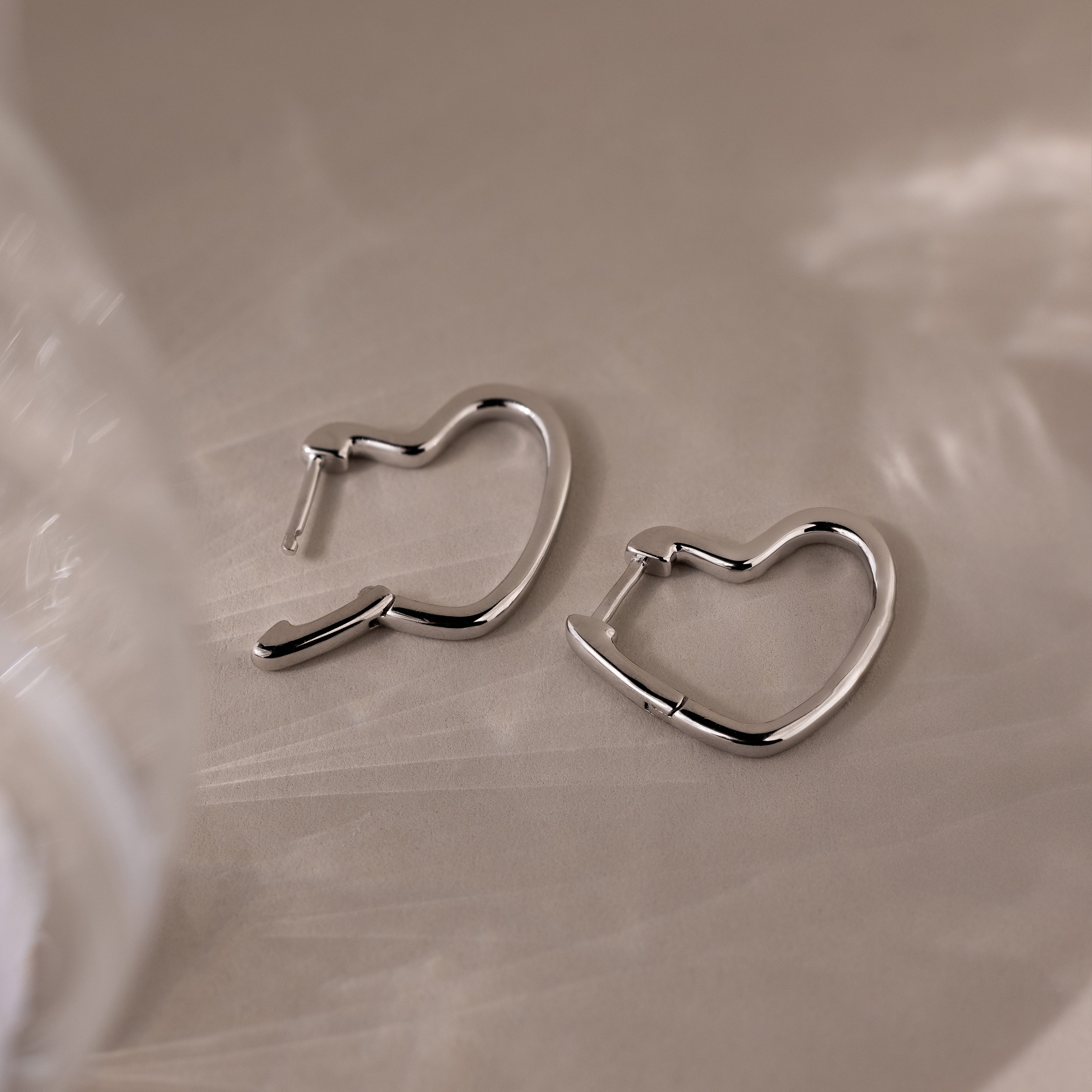 Heart-shaped silver hoop earrings on a beige surface