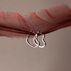 Two silver hoop earrings on a red fabric background