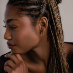 Close-up of a woman with braided hair wearing a small heart shaped silver hoop earring.