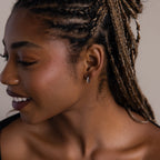 Close-up of a woman with braided hair wearing a small silver diamond hoop earring.