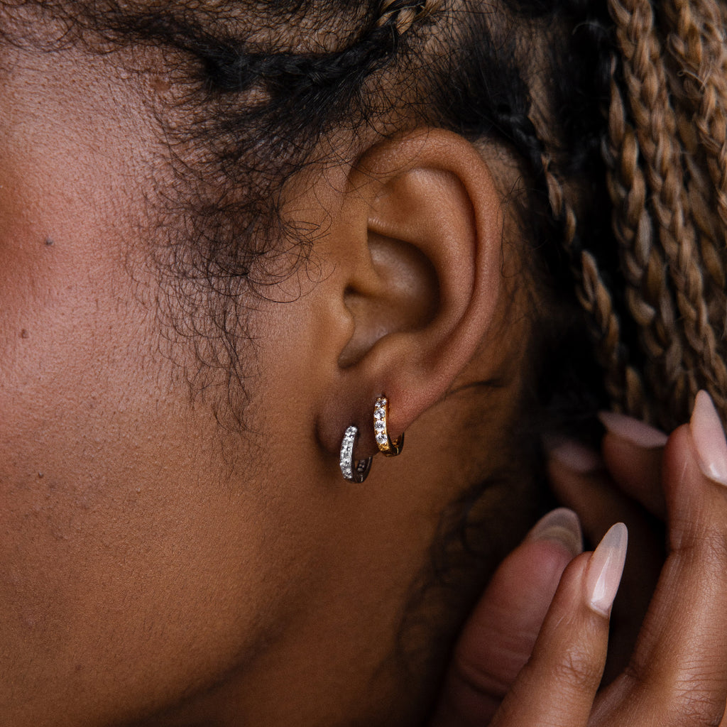 Close-up of an ear with two silver and gold hoop earrings and a hand adjusting hair.