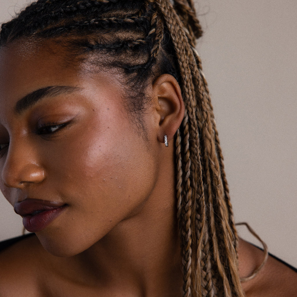 Close-up of a woman with braided hair wearing a silver diamond earring against a neutral background