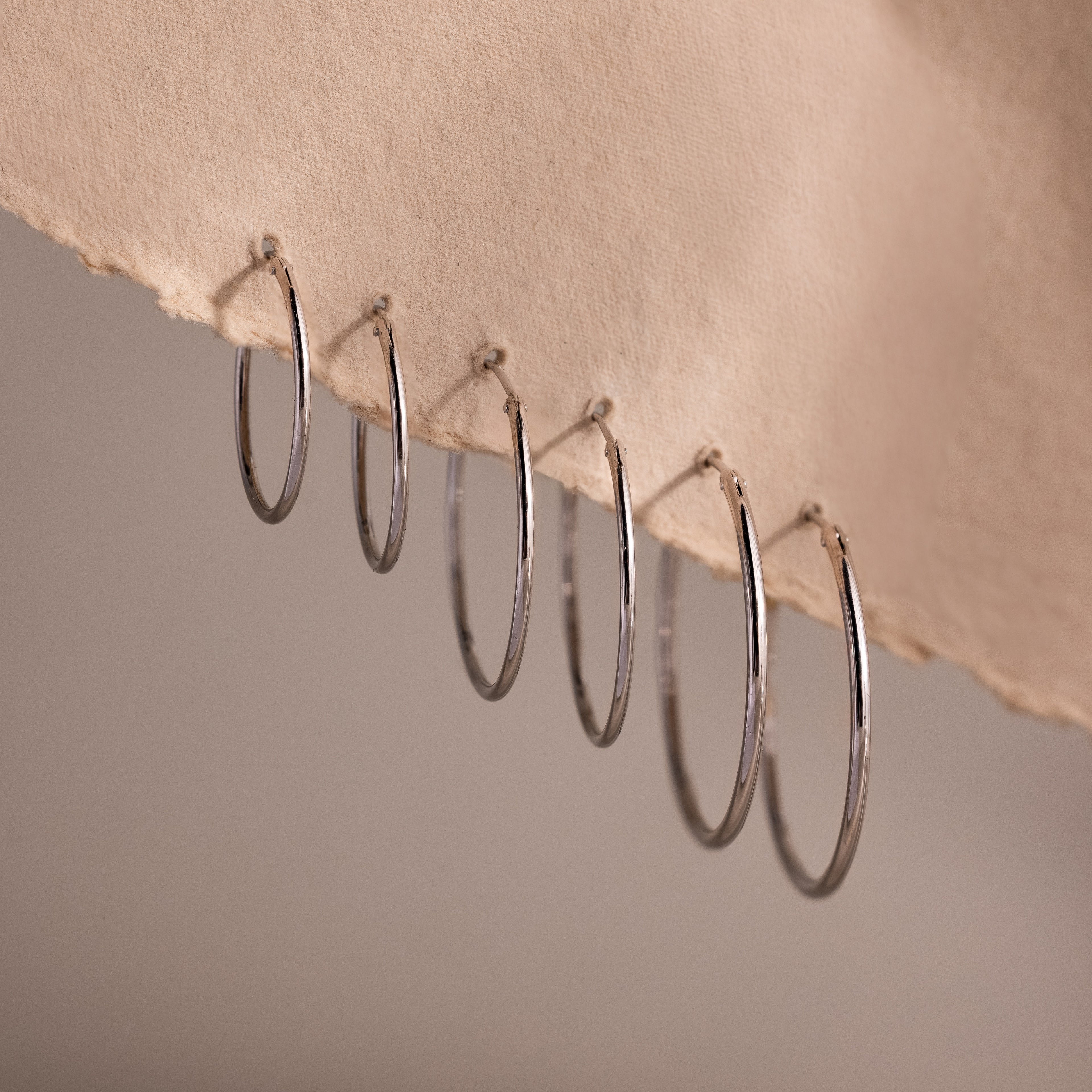 Set of three different sizes of silver hoop earrings on a textured beige surface