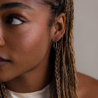 Close-up of a person with braided hair wearing a silver hoop earring.