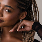 Close-up of a woman with braided hair wearing silver diamond dangle hoop earrings.