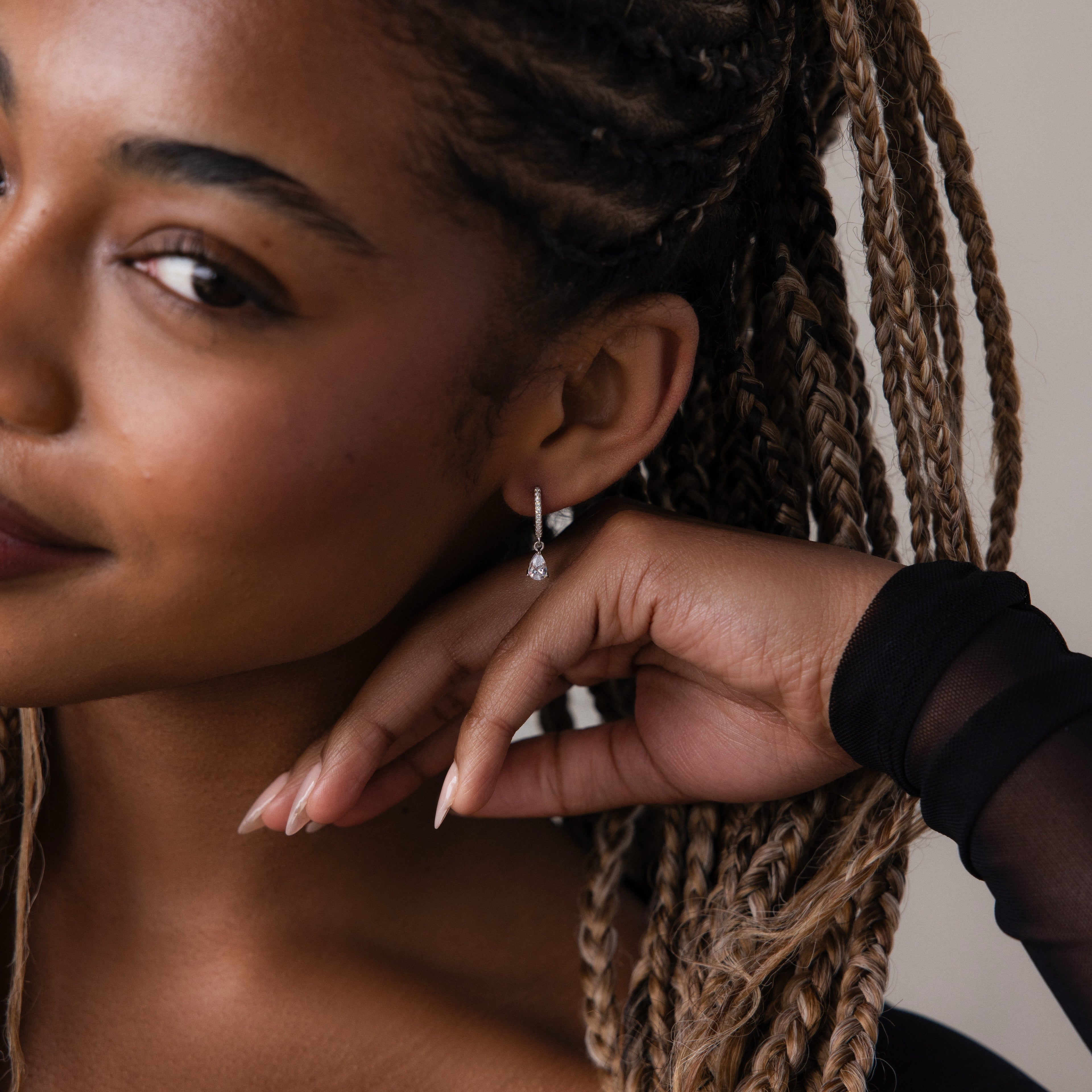 Close-up of a woman with braided hair wearing silver diamond dangle hoop earrings.