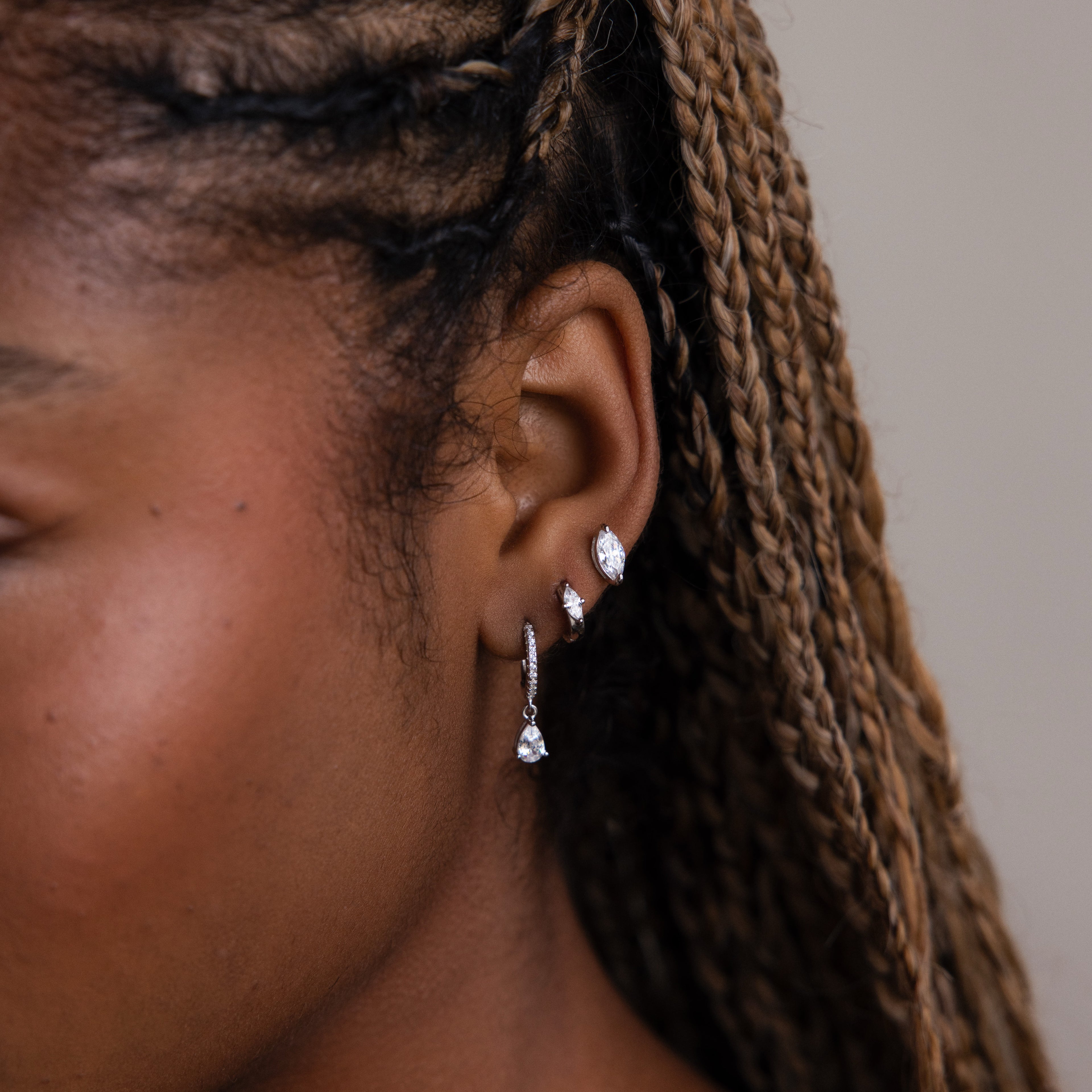 Close-up of a person's ear with multiple diamond earrings against a neutral background