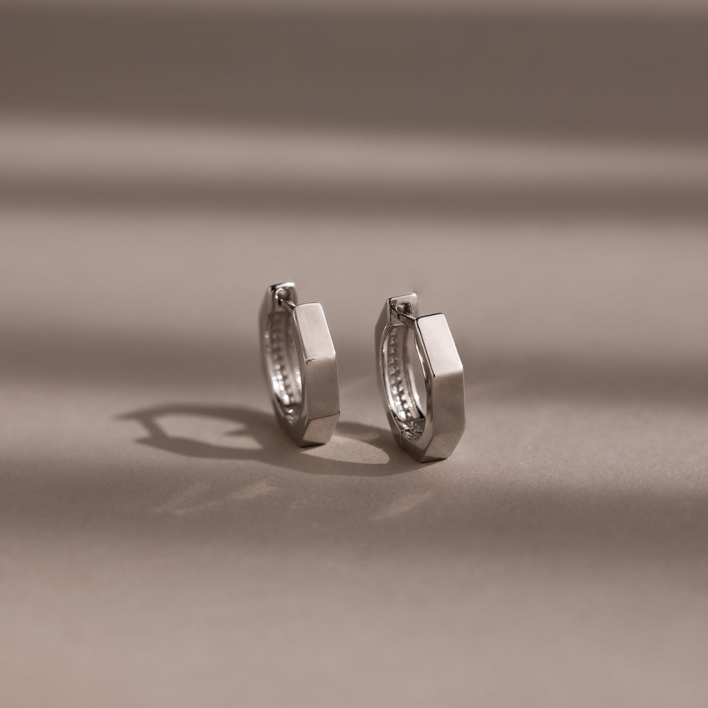 Pair of silver huggie hoop earrings on a beige background
