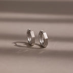 Pair of silver huggie hoop earrings on a beige background