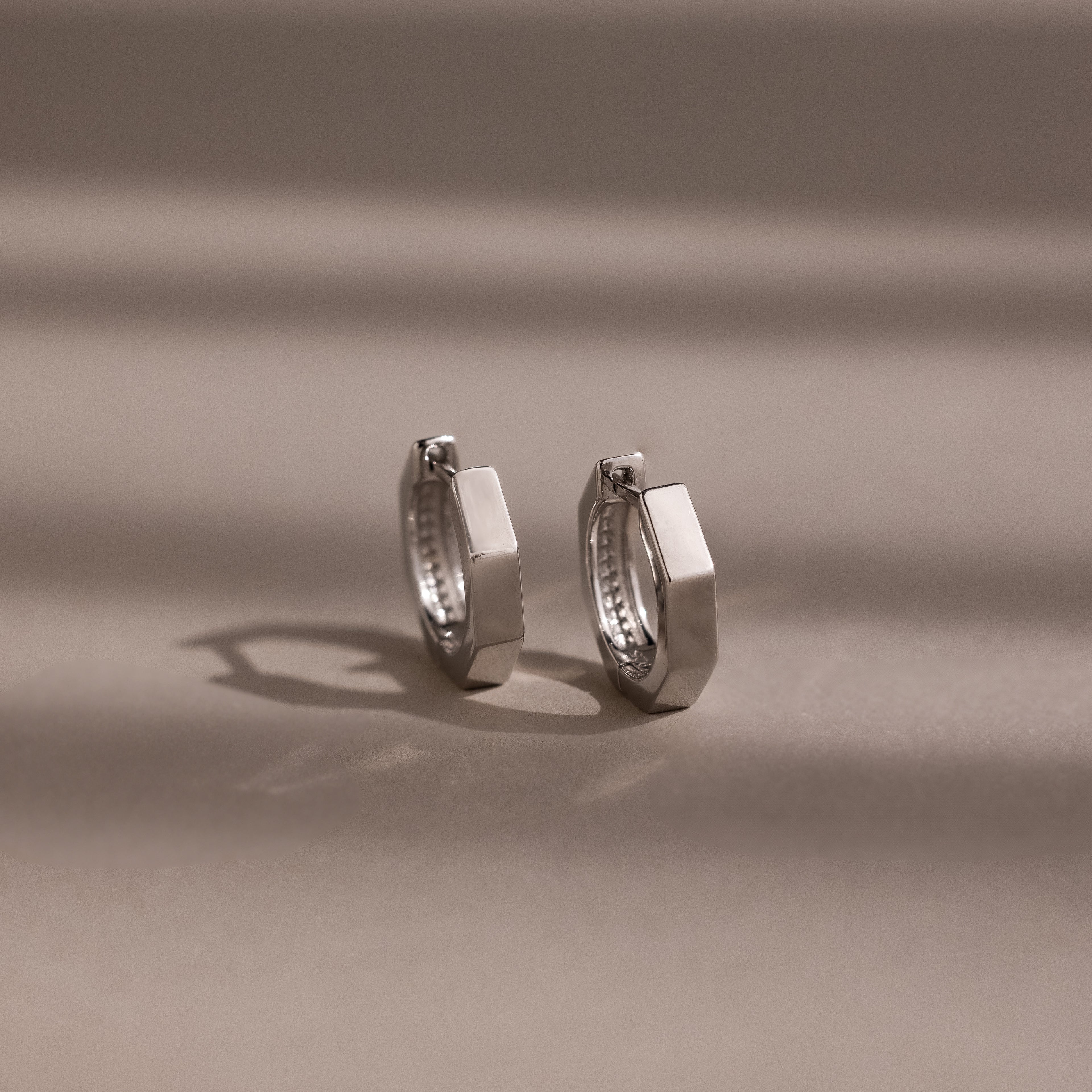 Pair of silver huggie hoop earrings on a beige background