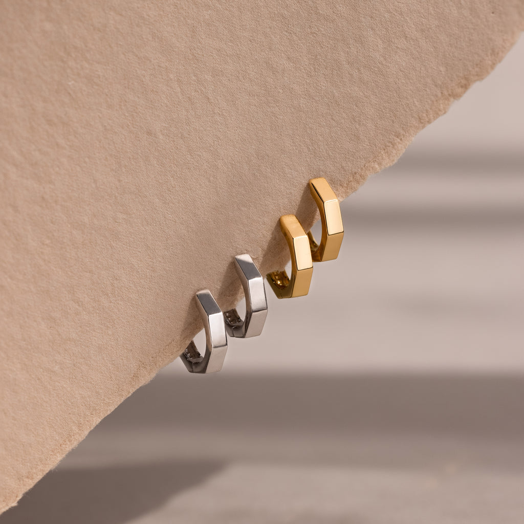 Two gold and silver hoop earrings on a beige background