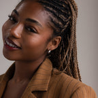 Woman with braided hair wearing silver hoop earrings and a brown pinstripe blazer against a neutral background