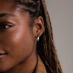 Close-up of a woman's ear with a silver hoop earring against a neutral background