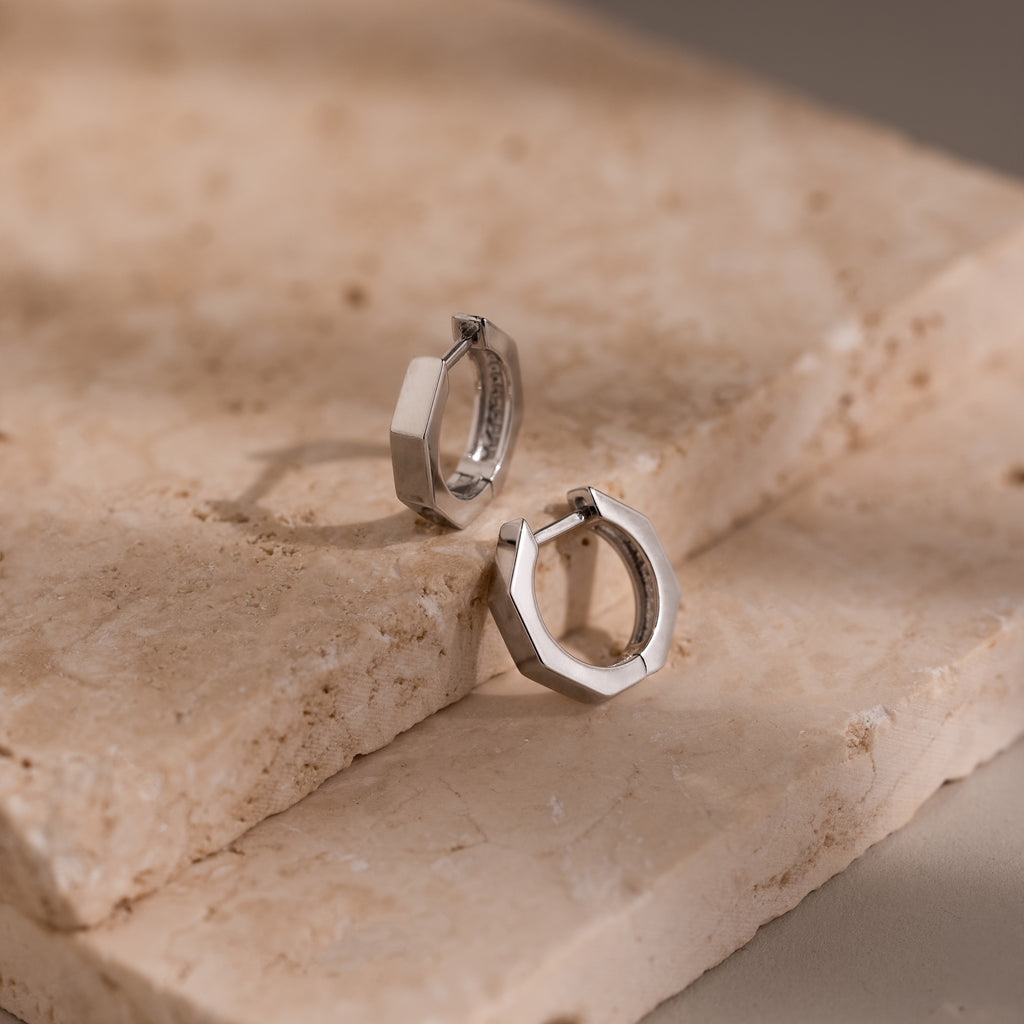 Geometric silver hoop earrings on a textured stone surface