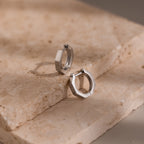 Geometric silver hoop earrings on a textured stone surface