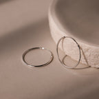 Two silver hoop earrings on a beige surface with a textured bowl in the background.