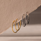 Two pairs of hoop earrings, one set of gold and one set of silver, hanging from a beige fabric surface.