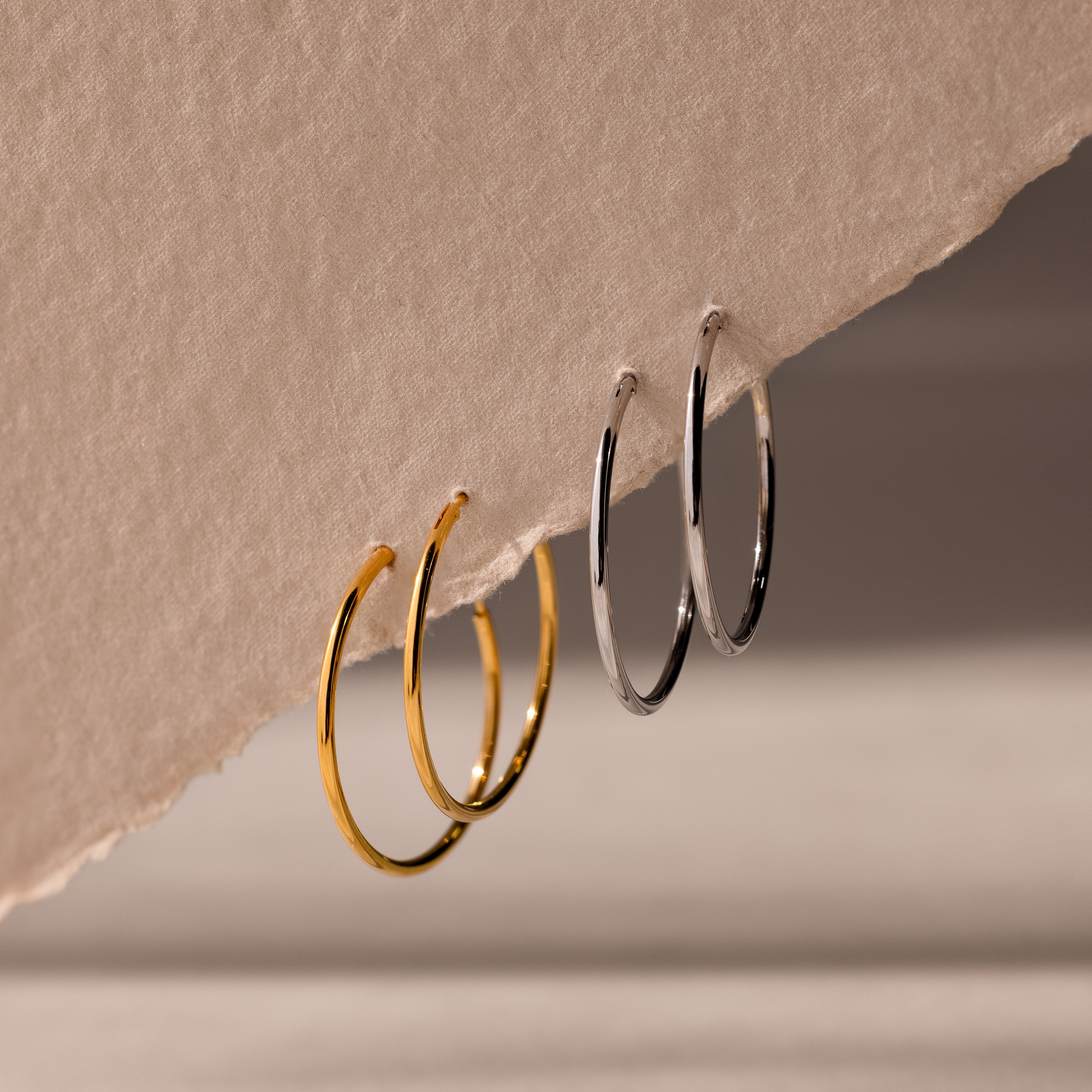 Two pairs of hoop earrings, one set of gold and one set of silver, hanging from a beige fabric surface.