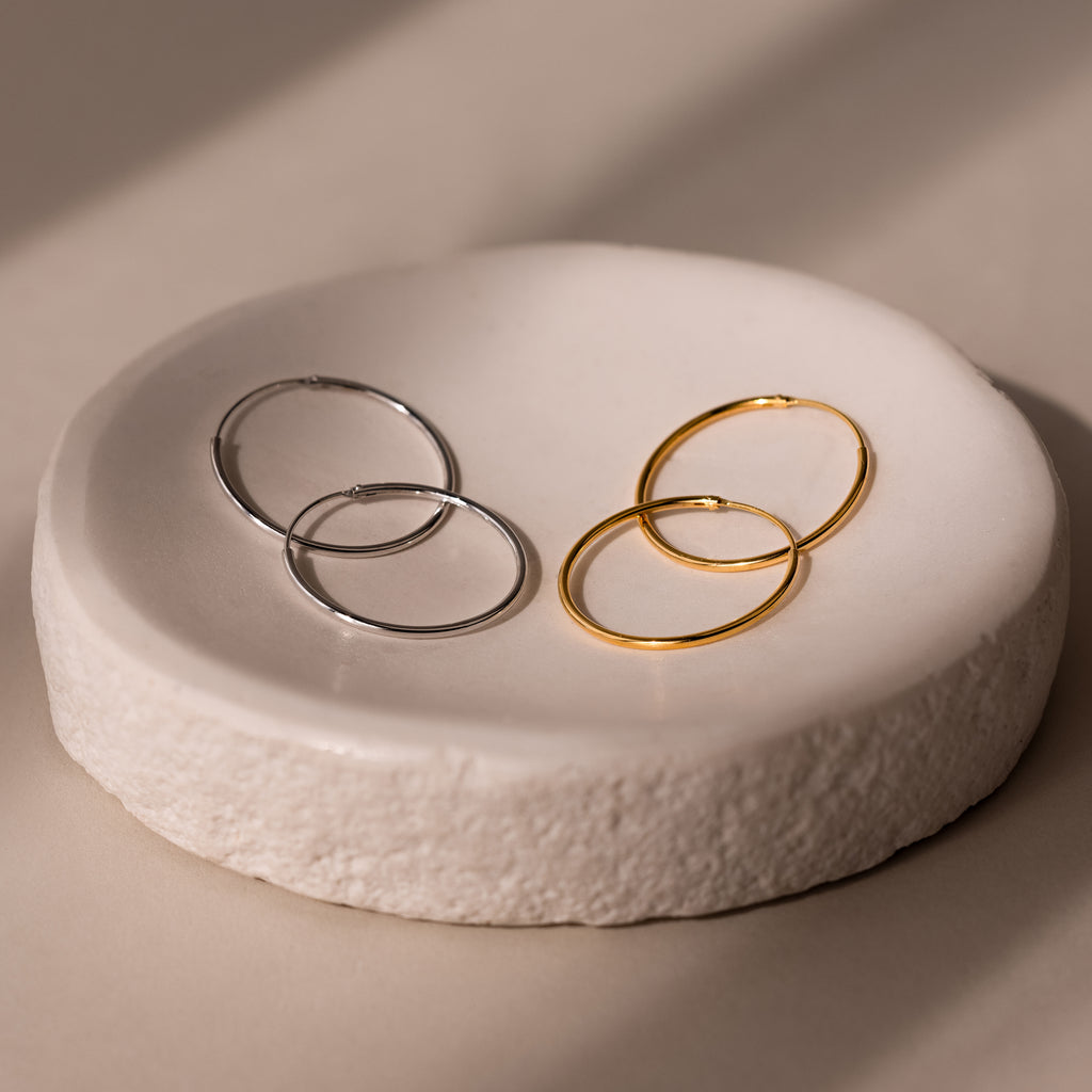 Two pairs of gold and silver hoop earrings on a textured white stone surface.