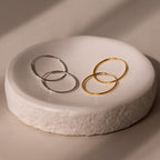 Two pairs of gold and silver hoop earrings on a textured white stone surface.